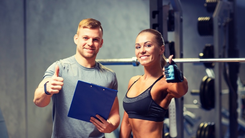 Happy personal trainer with client with thumbs up in gym. 