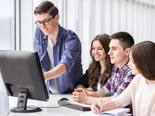four students sat at desk looking at computer screen