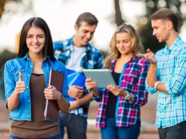 four students standing outside looking at tablet