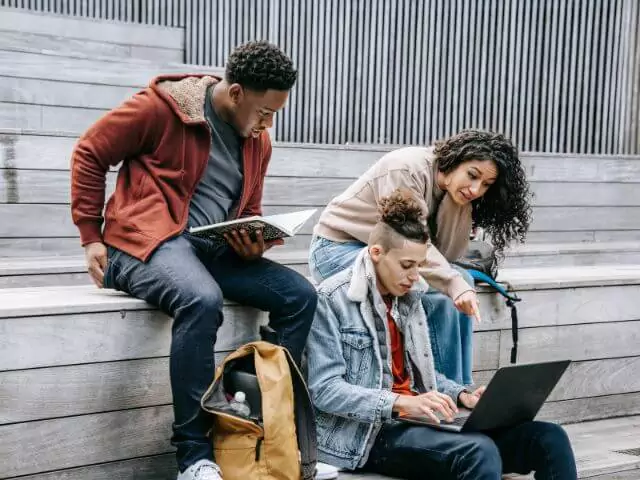 three students sitting on steps looking at laptop