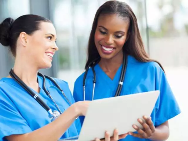 two nurses smiling and looking at laptop