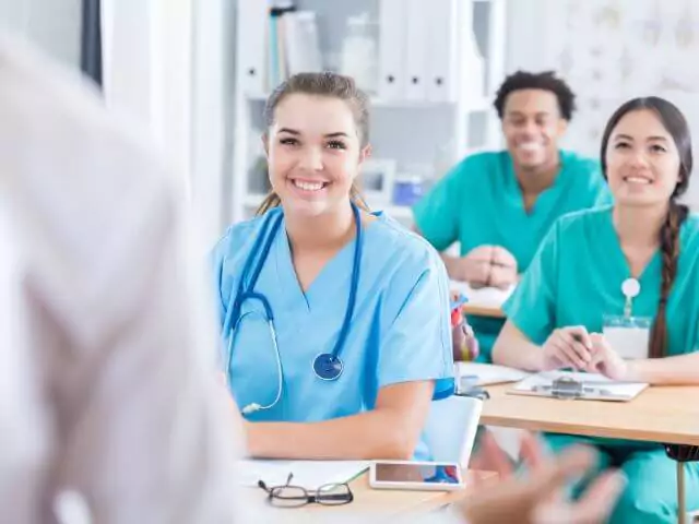 3 nurses sitting at desks listening to teacher