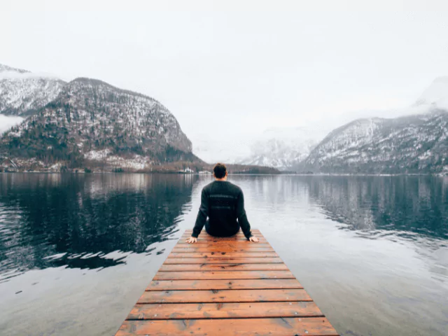 Man Sitting On Dock Looking At Mountains