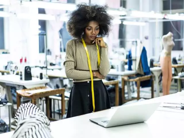 fashion designer looking at laptop with tape measure around neck