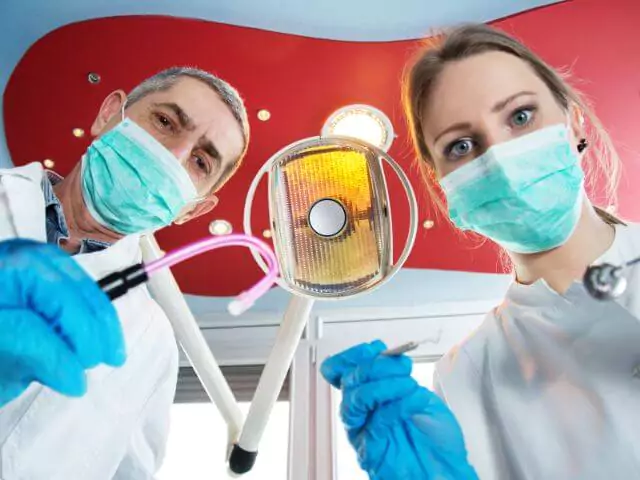 dentist and dental nurse holding instruments looking at camera