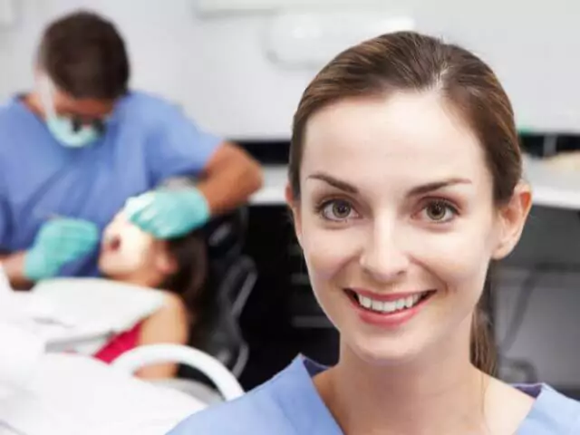 dental nurse looking at camera while dentist works in background