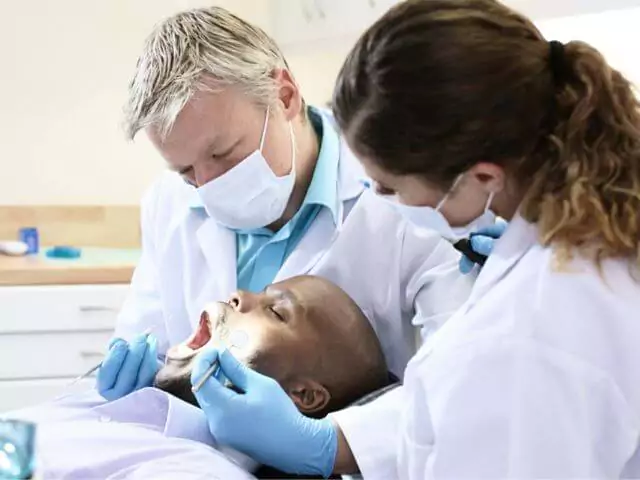 dentist examining patients teeth whilst dental nurse watches