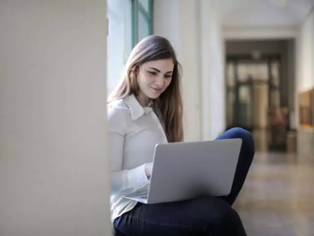 woman sat with laptop in library corridor