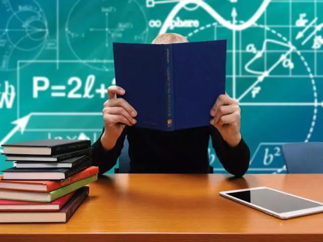 Person Reading Book Sat At Desk