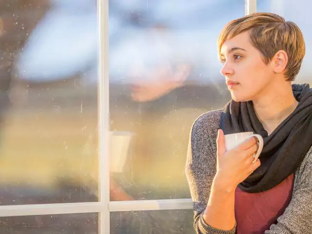 Woman Looking Out Of Window Holding Tea Cup