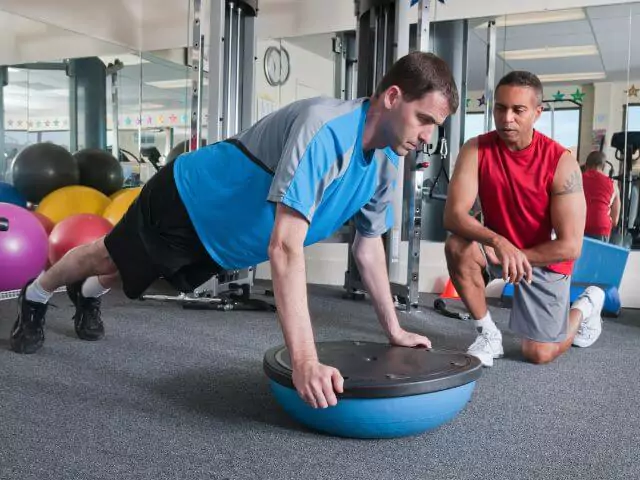 personal trainer teaching client on balance board