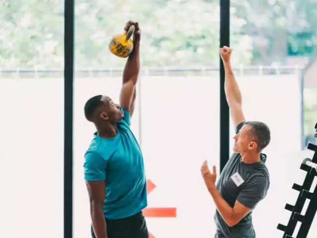 personal trainer helping client workout with kettle bells