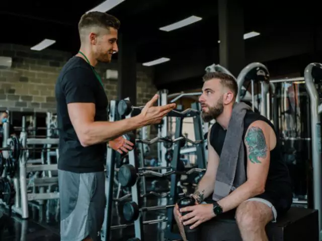 male personal trainer teaching student to use weight equipment