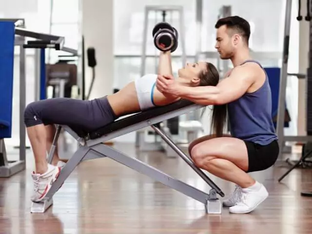 male personal trainer with female student lifting weights on bench