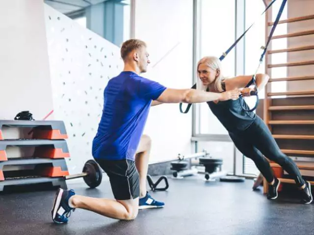 personal trainer helping client doing rope exercises