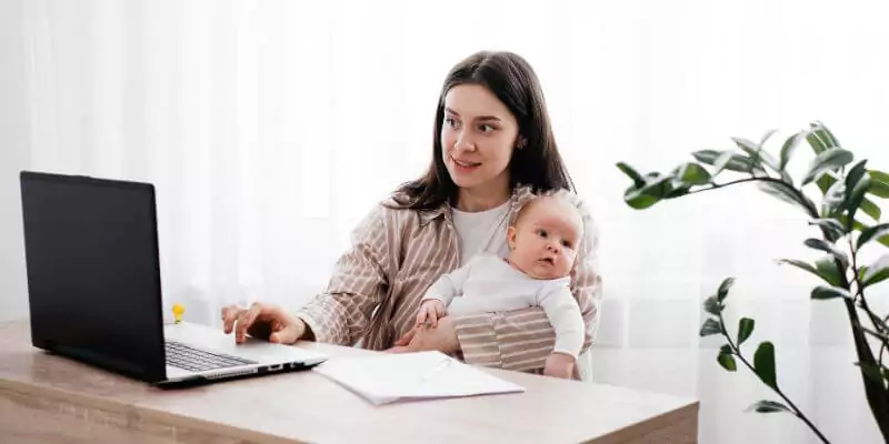 woman holding a baby studying on laptop