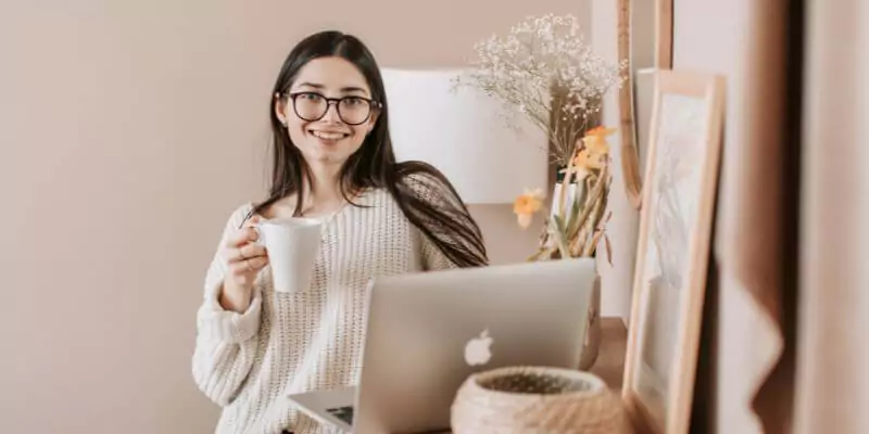 woman smiling at camera holding a laptop and drink