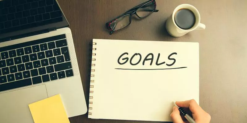 student writing goals on notepad next to laptop on desk