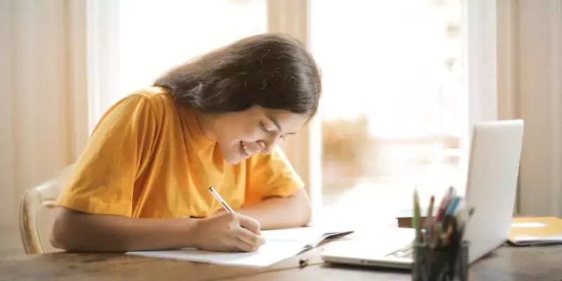young woman writing whilst studying on laptop