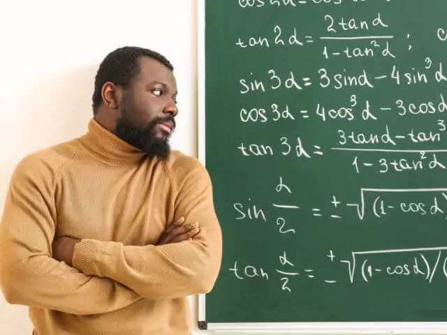 maths teacher looking at chalkboard containing maths symbols