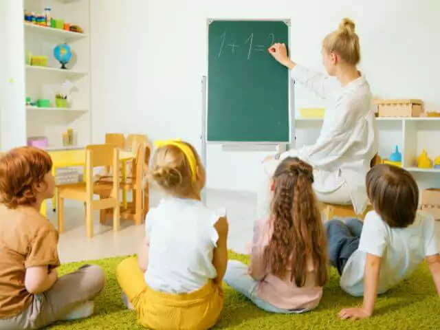 maths teacher writing on chalkboard for group of children