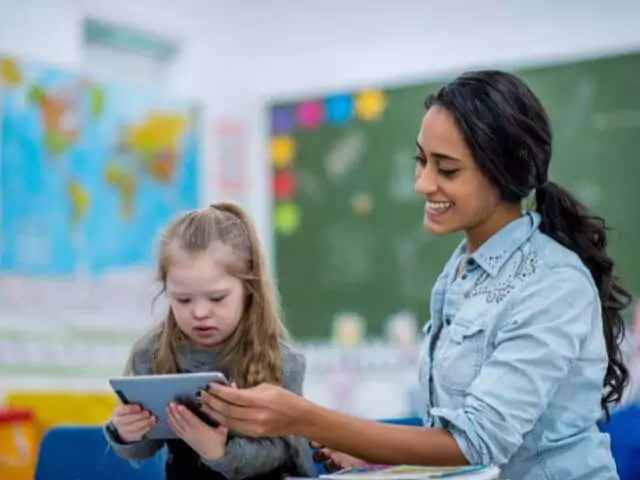 teaching assistant helping pupil with tablet